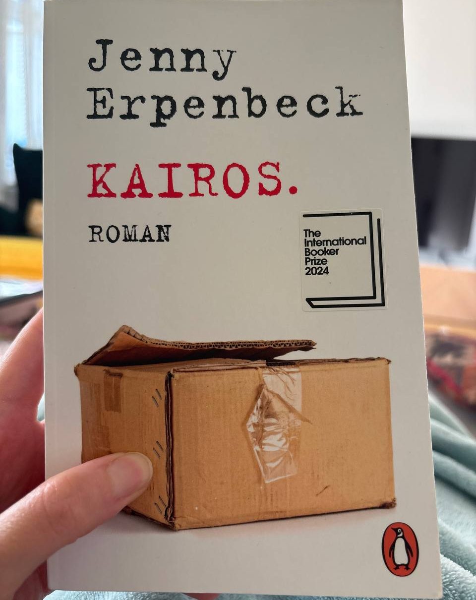 Mann in Anzug mit roter Krawatte, stehend vor einer Weltkarte im Hintergrund.